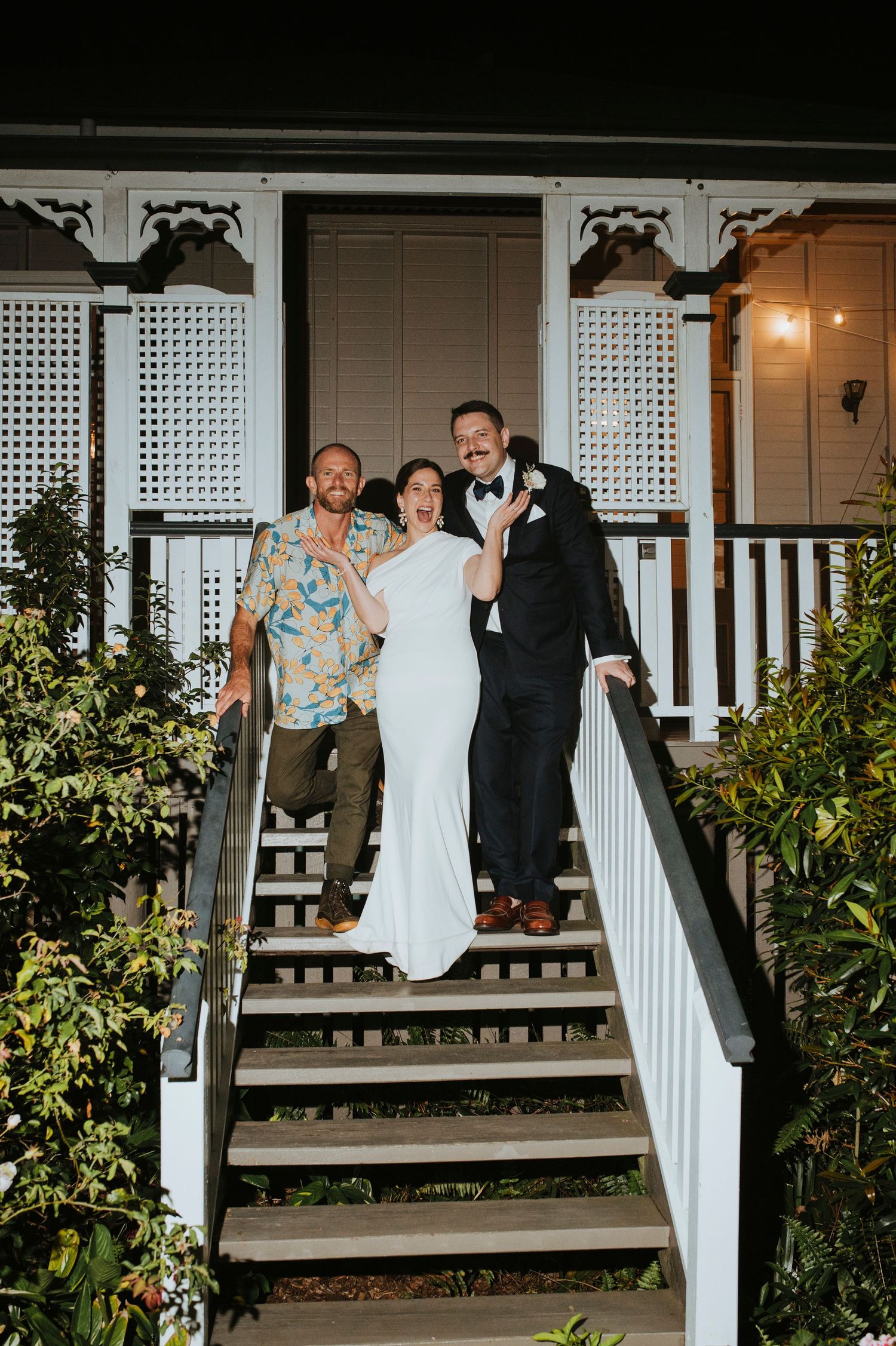 Wedding party posing on white porch of elegant house with lattice details.