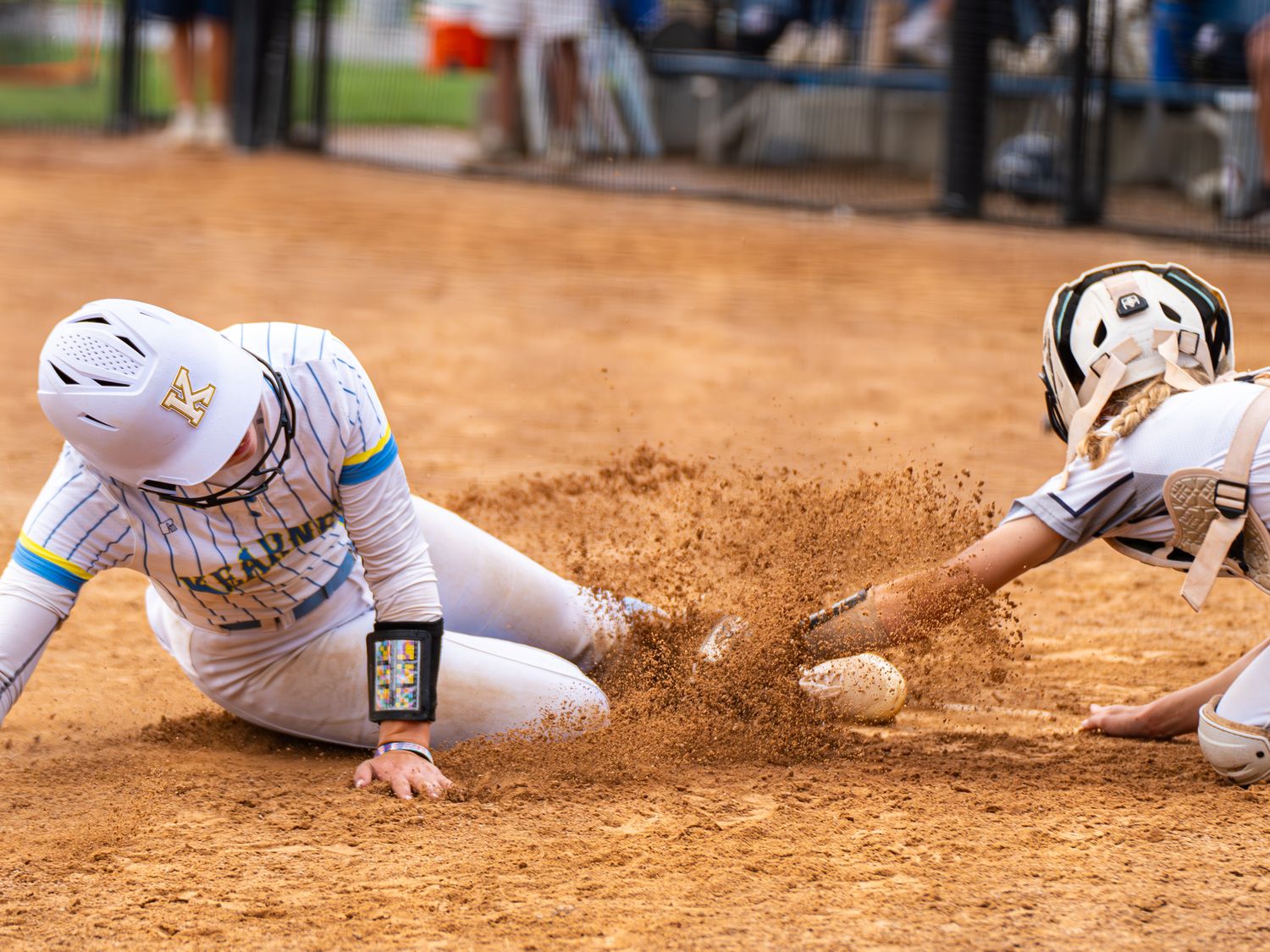 Two softball players sliding into base creating dust cloud during intense play.
