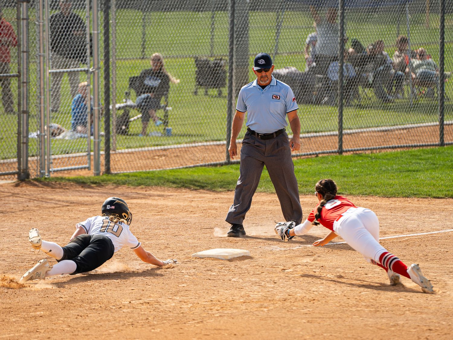 Softball players slide into base as umpire watches close play.