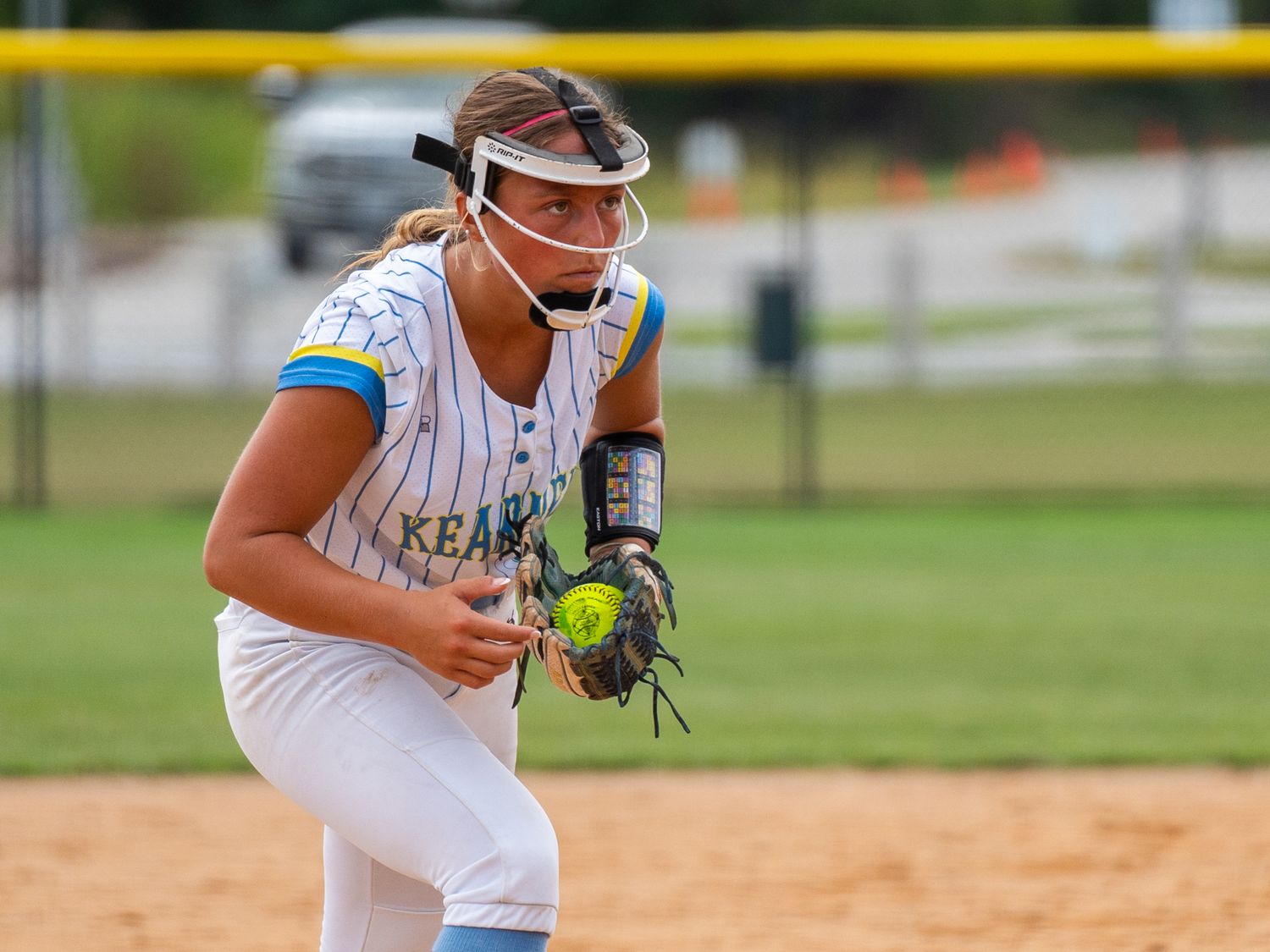 Softball pitcher in white uniform prepares to throw pitch during game.