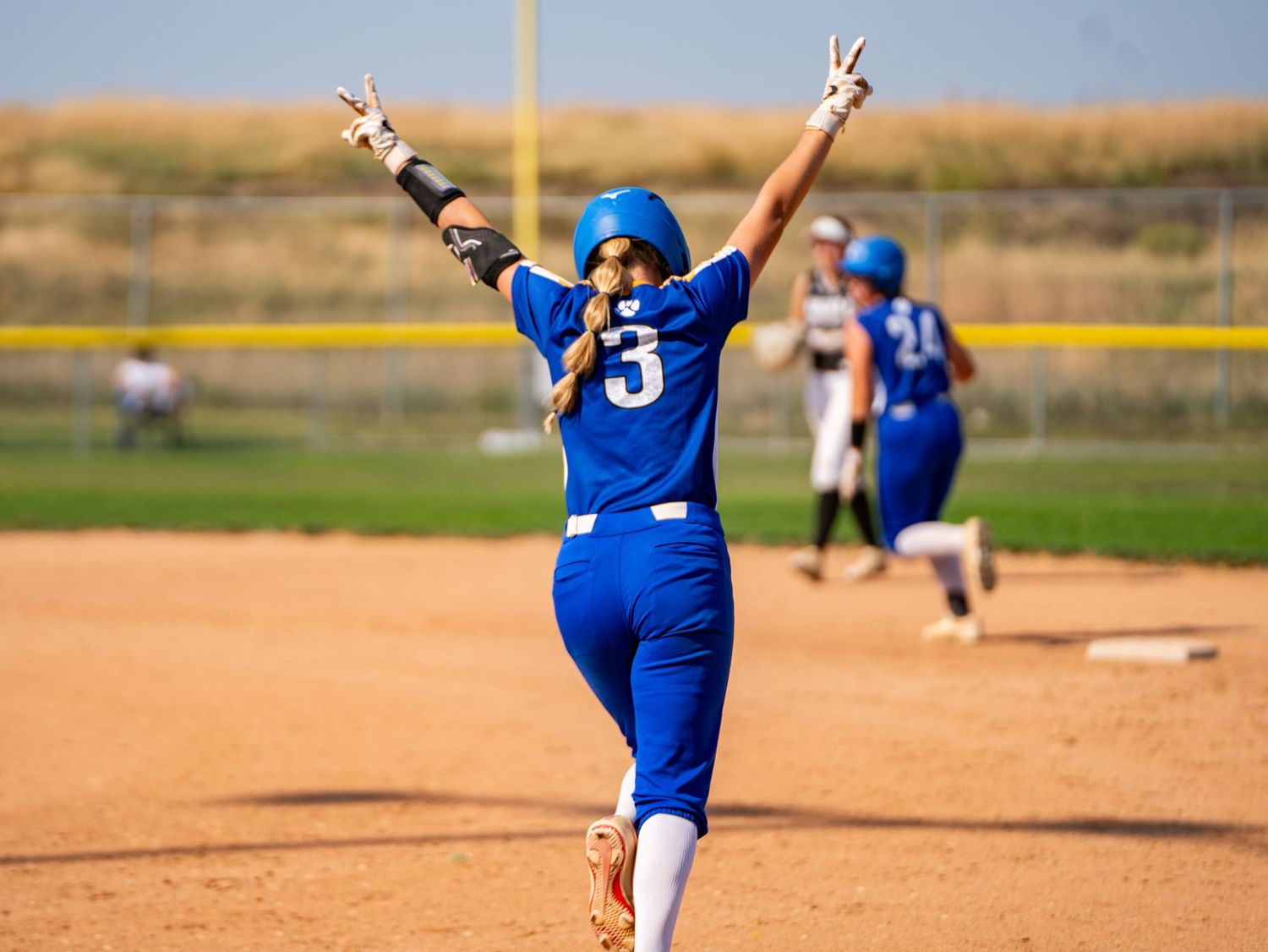 Softball player in blue uniform celebrates with victory signs on the field.