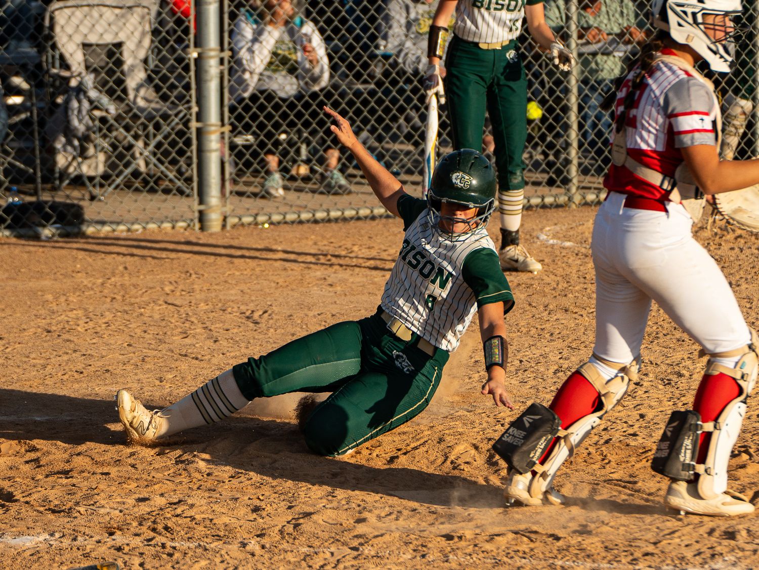 Dramatic sliding play at home plate between players in green and red uniforms.