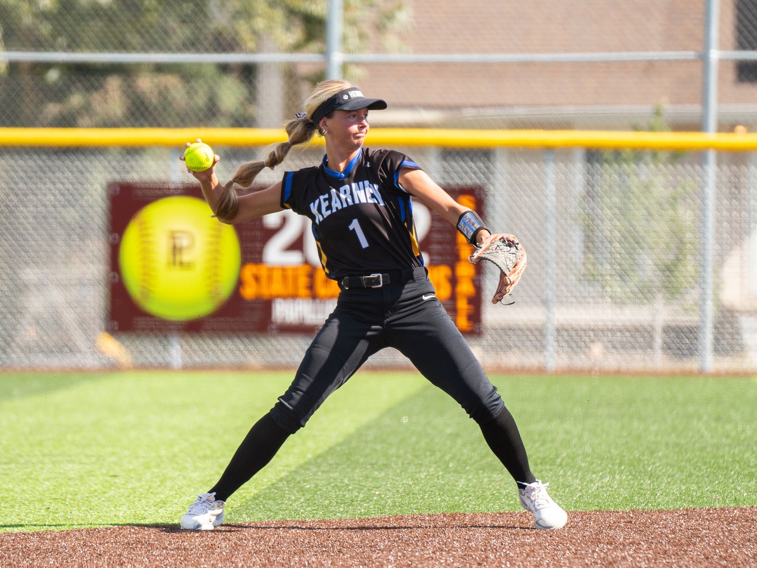 Softball pitcher in black uniform winds up to throw on grass field.