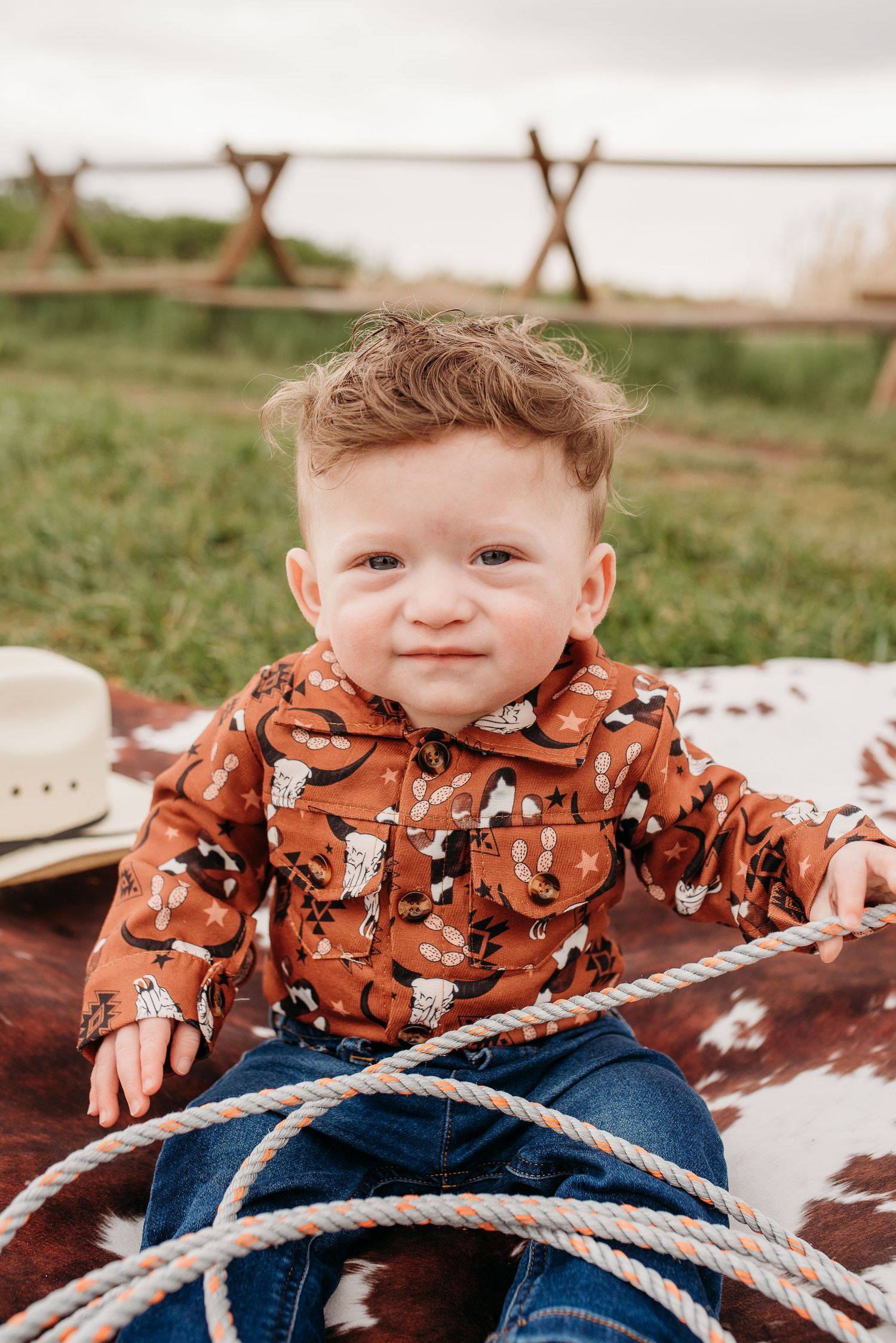 Young child in orange patterned shirt sitting on western-style blanket with rope.
