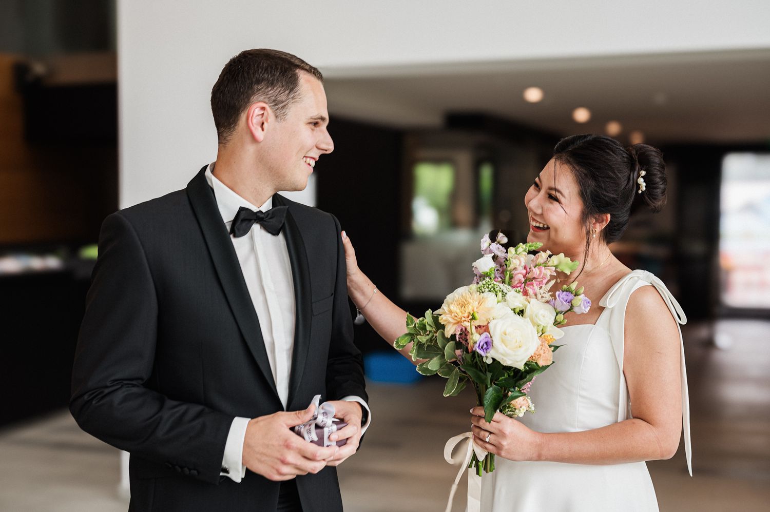 Happy couple smiling at each other during first look moment with bride holding white and pink floral bouquet.