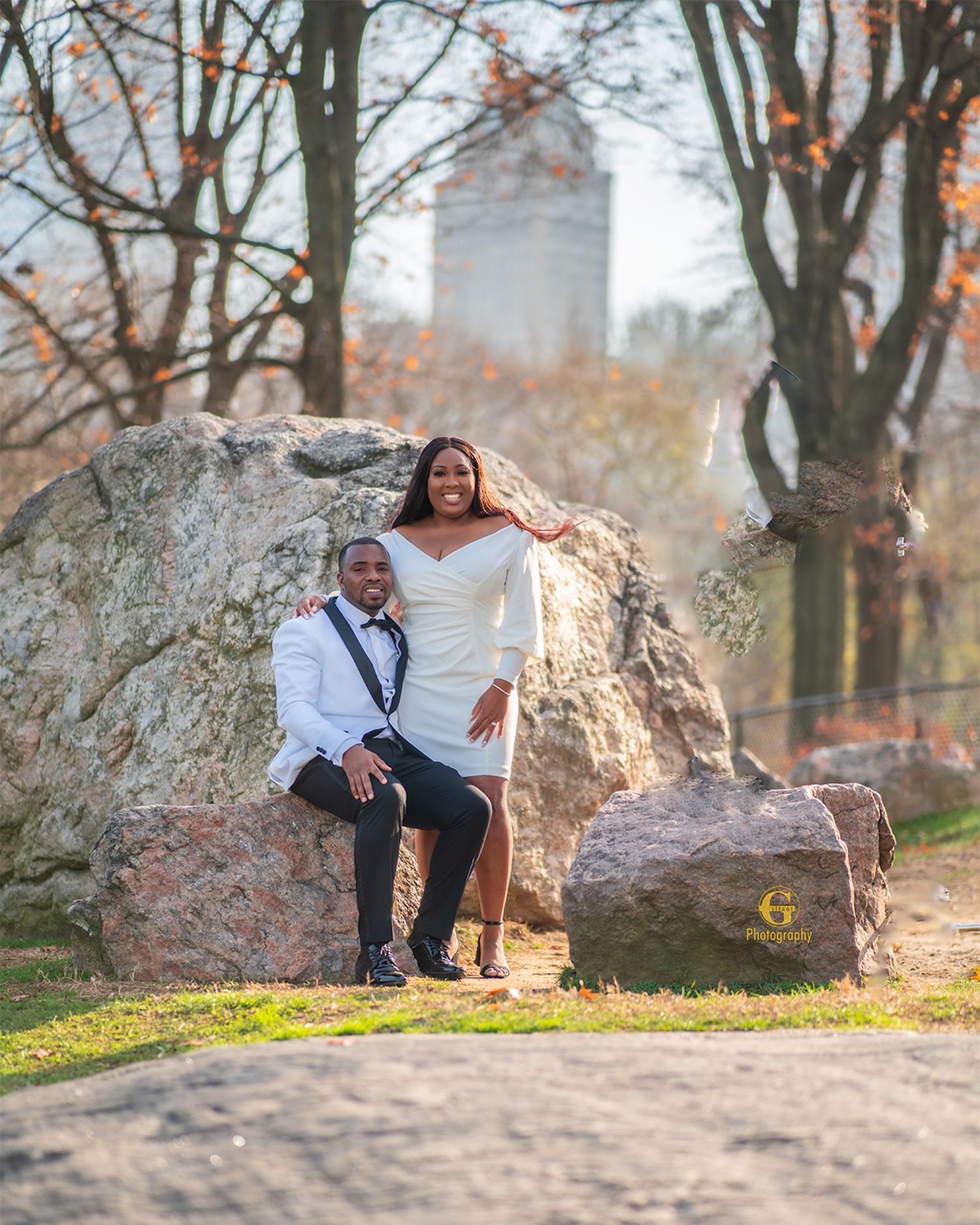 Couple in formal wear poses on large rock formation during outdoor photoshoot.