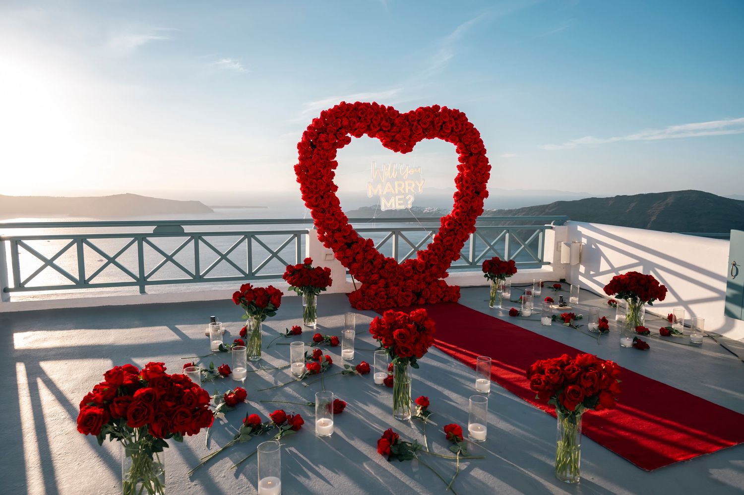 Red rose heart arch and scattered petals create romantic proposal setting on Santorini terrace.