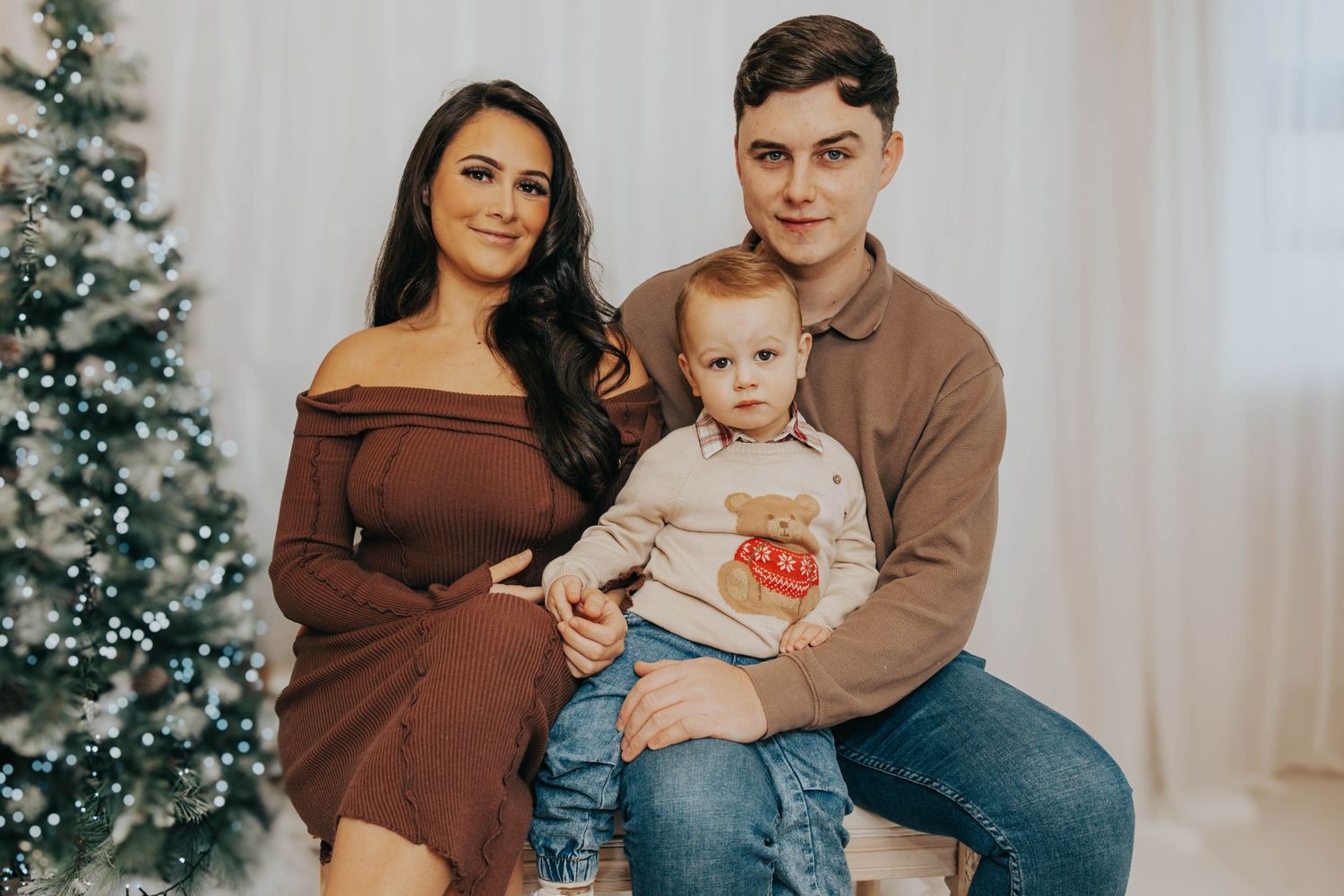 Winter indoor family portrait with brown and neutral tones next to Christmas tree.