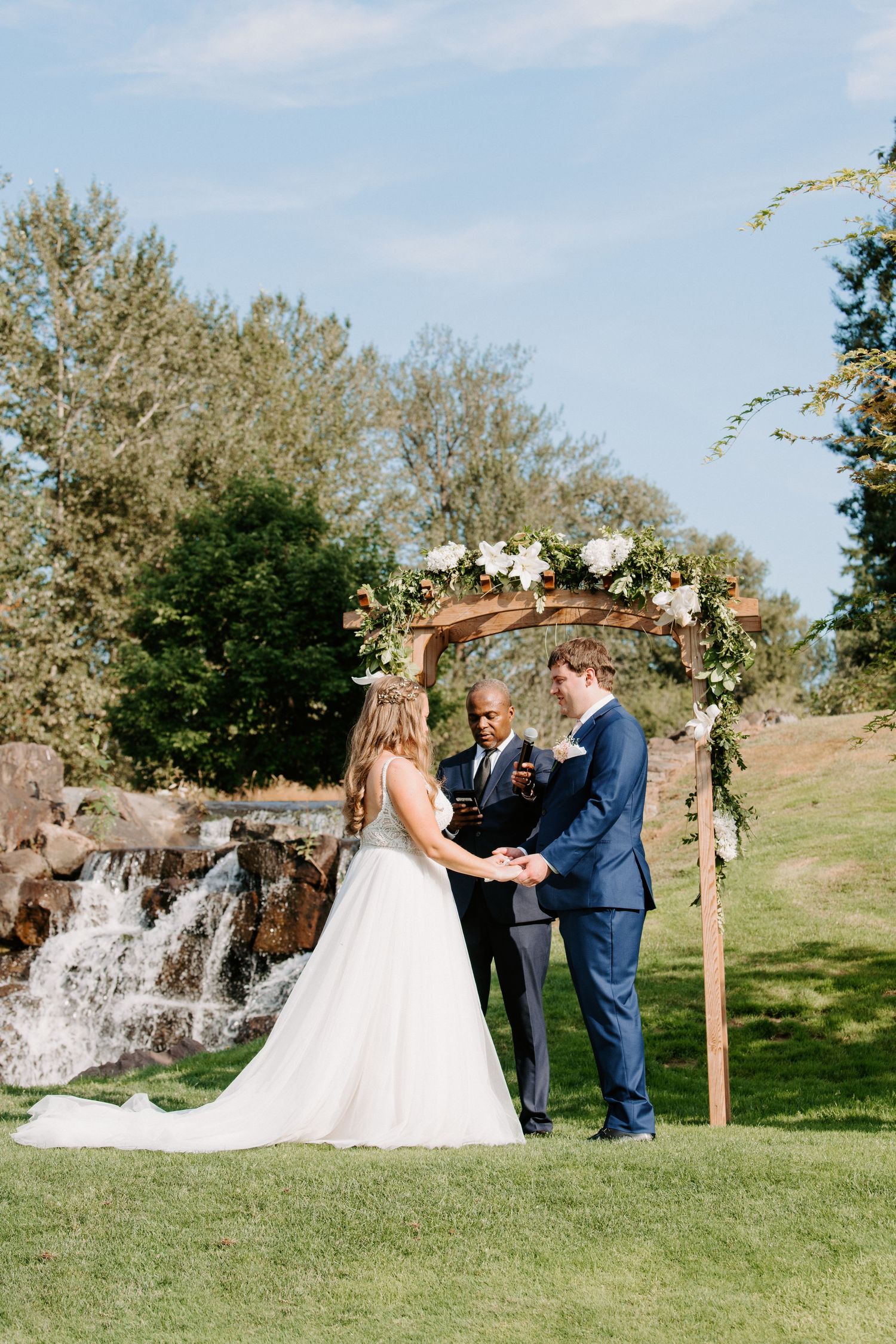 Wedding ceremony setup with wooden arch decorated with white flowers in front of a waterfall.