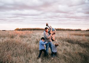 Joyful family playing together in a golden grass field under a cloudy sky.