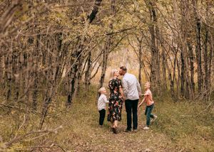 Family of four walking through an autumn forest path surrounded by colorful foliage.