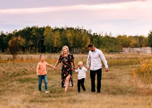A happy family of four walks hand in hand through a scenic autumn field at sunset.