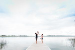Children playing with a ball on a wooden dock over a calm lake under a cloudy sky.
