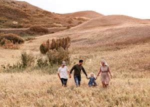 A family of four walks hand in hand through a golden autumn meadow with rolling hills.