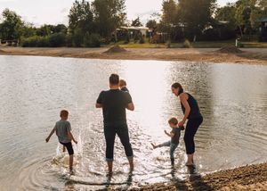 Family wading in shallow lake water on a sunny day near a sandy shore.