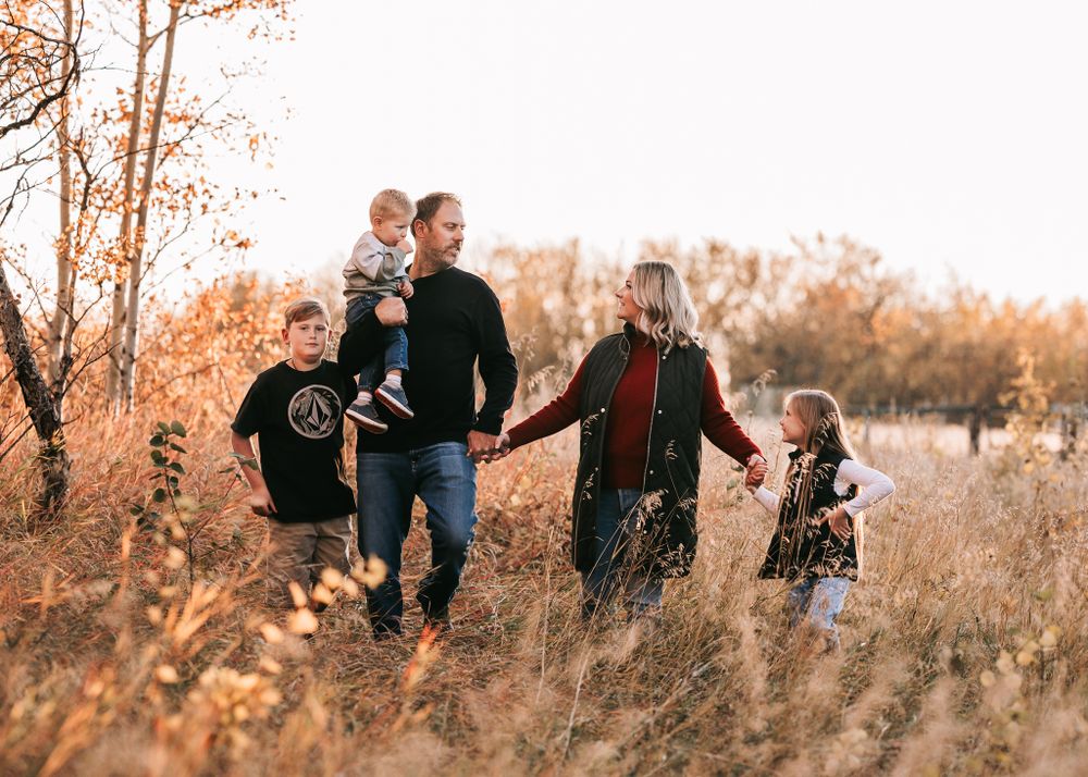 Family of five strolling through tall golden grass in autumn, holding hands at sunset.