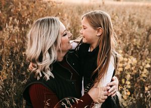 Mother and daughter sharing a tender nose-to-nose moment in a sunlit field of wildflowers.
