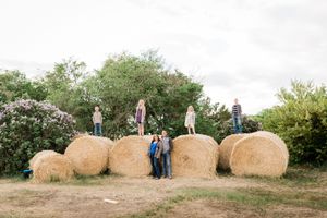Family posing with large round hay bales in a farm field on a cloudy day.