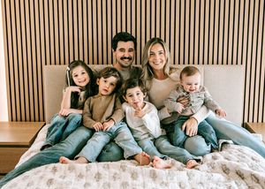 Smiling family of seven posing together on a bed in a modern bedroom.