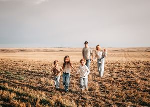 Family of five walking through a golden wheat field under a wide open sky on a sunny day.