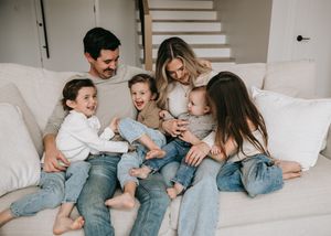 Happy family of six laughing together on a white couch in a bright living room.