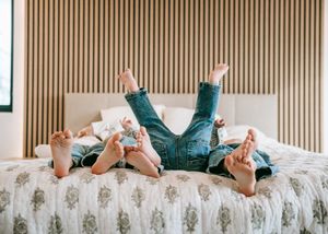 Two children lying on a bed with feet up in the air, wearing jeans, enjoying a playful moment together.