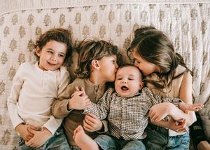 Four young siblings cuddling and kissing on a couch, sharing a sweet and joyful family moment.