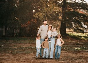 Happy family of six posing outdoors in autumn, parents with four children in coordinated neutral outfits.