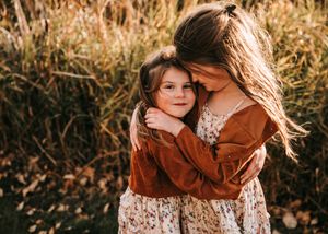 Two young girls in matching floral and rust outfits sharing a warm embrace.