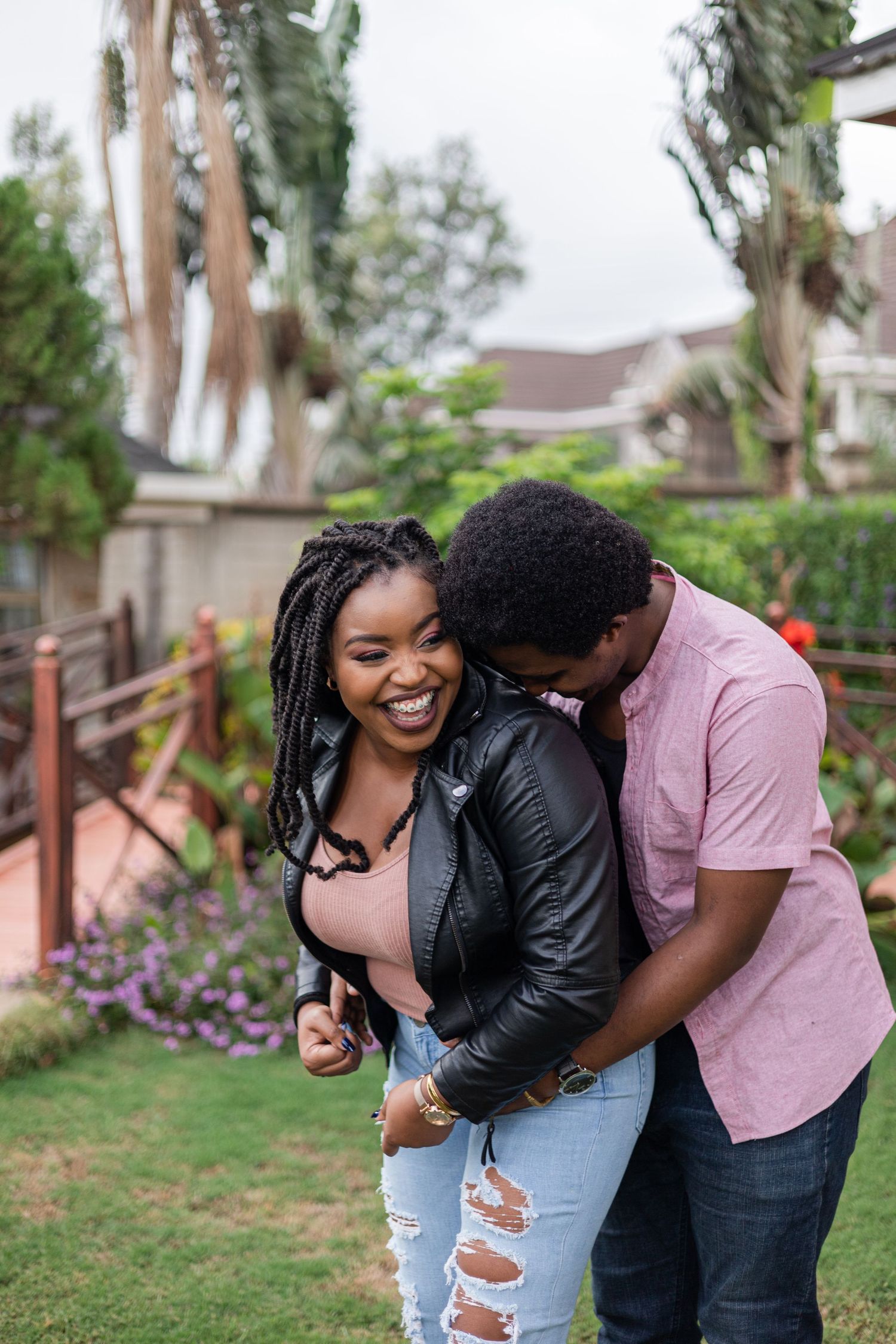 Couple's portrait in a garden. Man is hugging woman from behind. Woman is laughing. Ikigu George Photography.