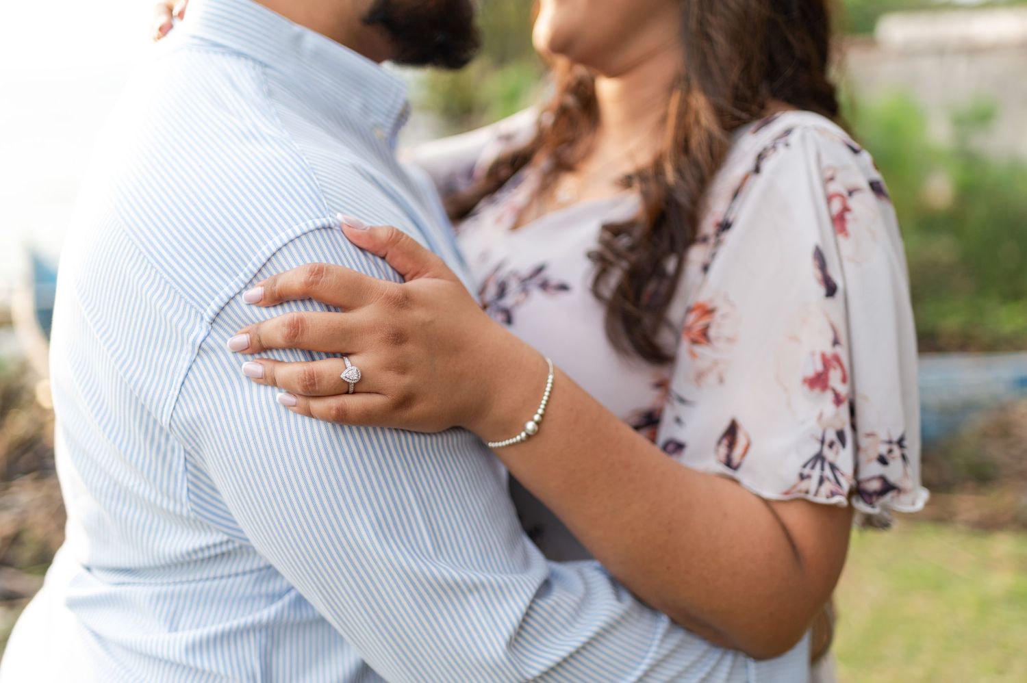 Engagement portraits of an Indian couple by Lake Victoria, Kenya. In a hug. She's holding him by his bicep. Big diamond ring on her finger.