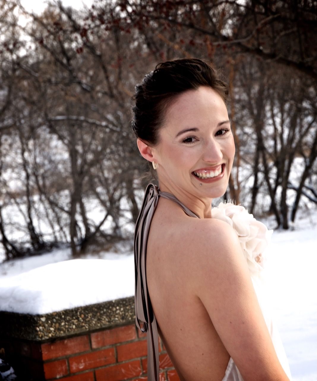 Joyful winter portrait shows a bright smile against a snowy outdoor backdrop with bare trees.