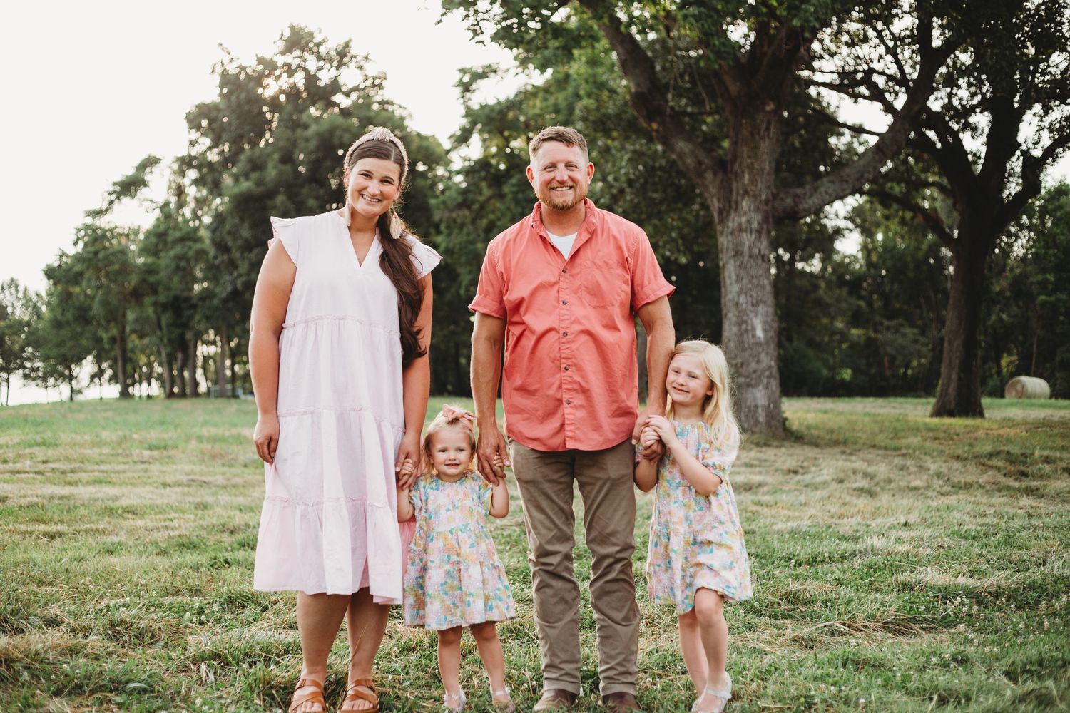 Family standing together outdoors in casual summer clothing on grassy hill.