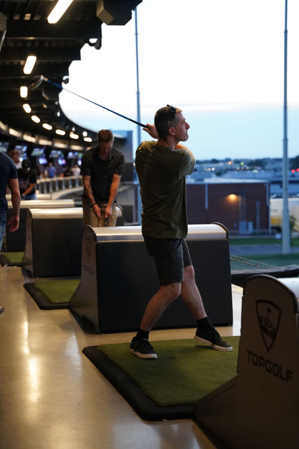 Person practicing golf swing at an indoor driving range bay.