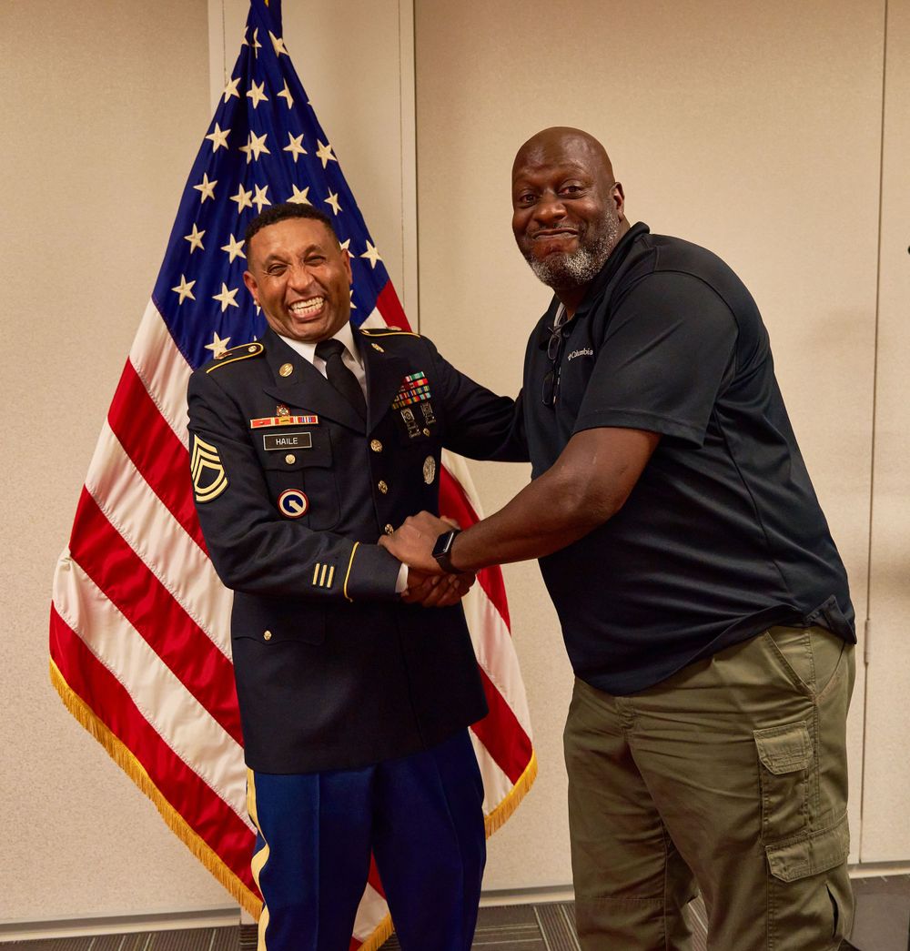 Two individuals share a celebratory moment in front of an American flag during a military ceremony.