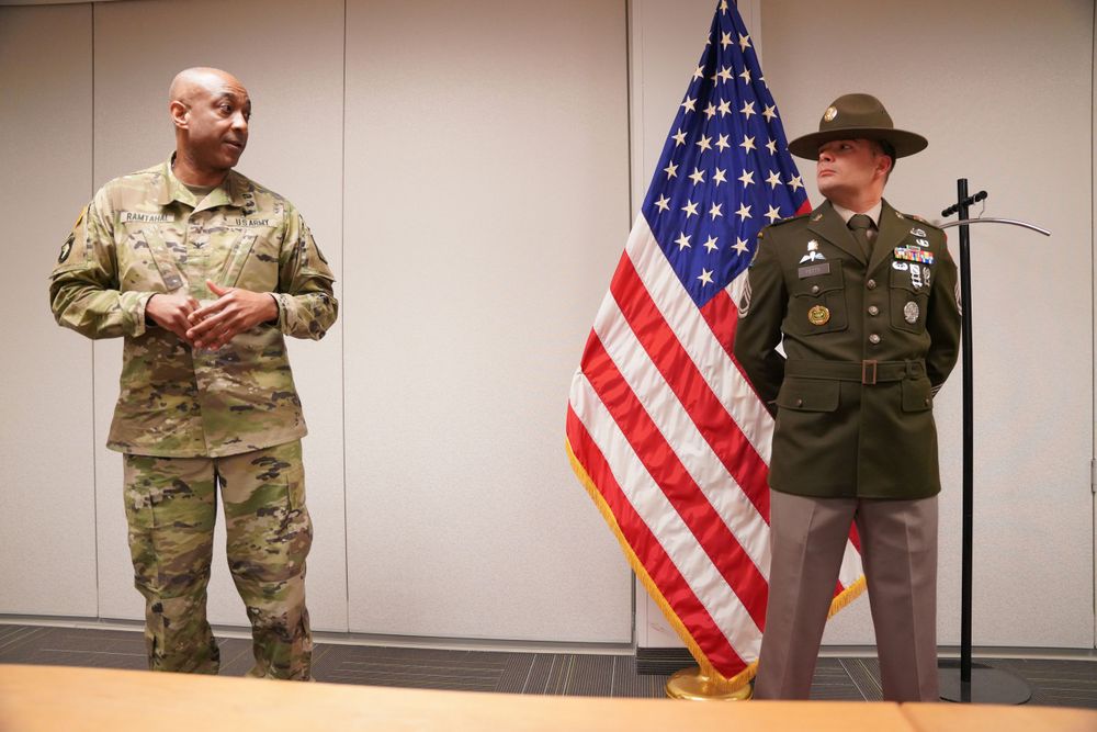 Two service members stand at attention next to an American flag during a military ceremony.