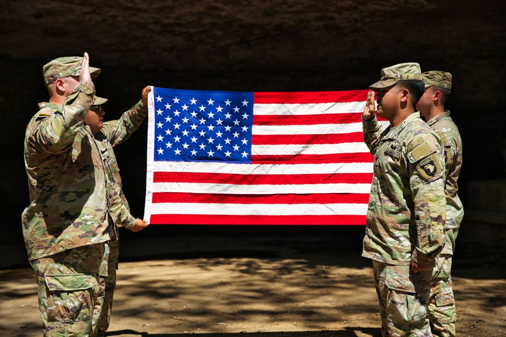 Military service members hold an American flag in a formal display ceremony.