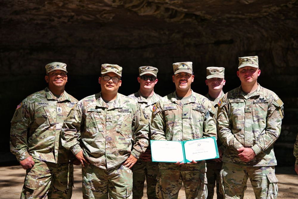 Group of soldiers in military fatigues pose together holding a certificate.