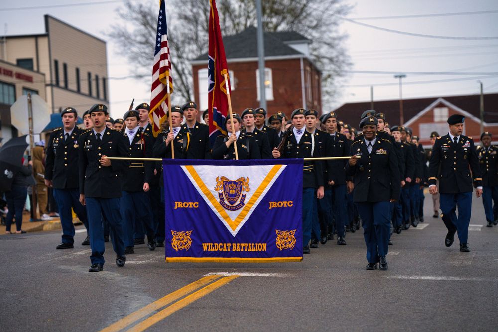 Military unit marches in formation carrying their unit colors during a parade.