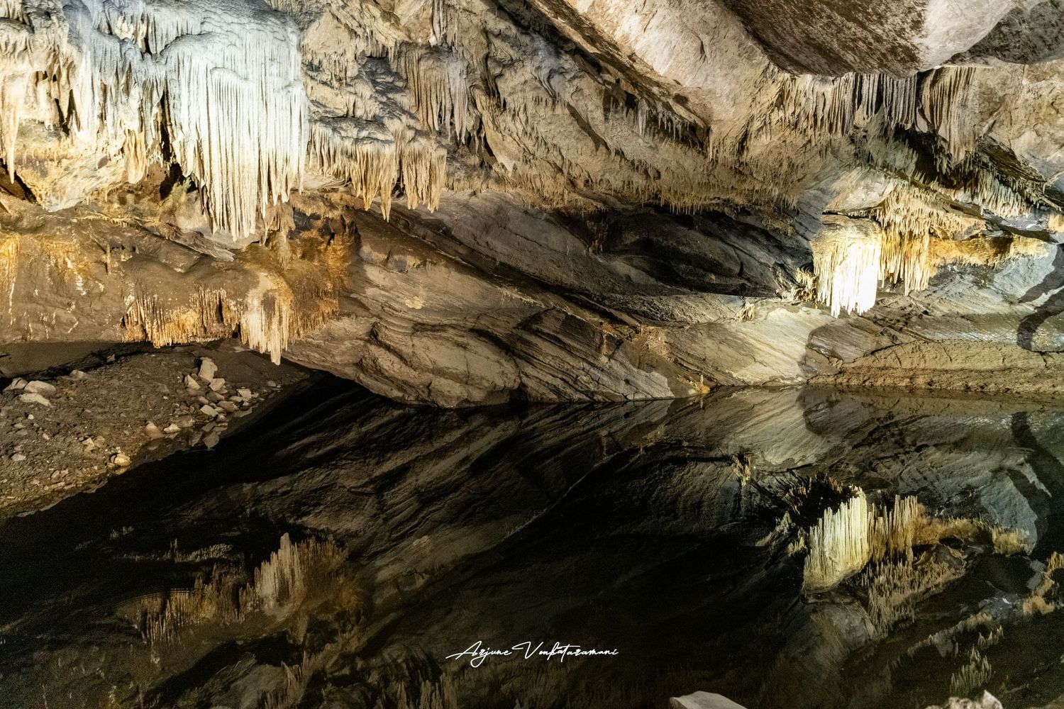 Stunning cave interior with stalactites reflected in still water, showcasing natural limestone formations in a dark grotto.