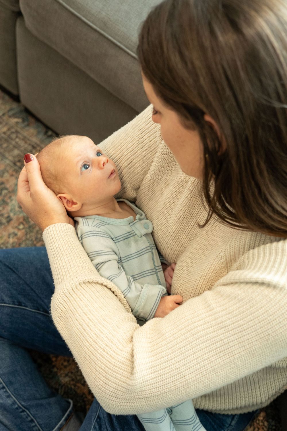 Tender moment between caregiver and infant wearing striped outfit while sitting on floor.