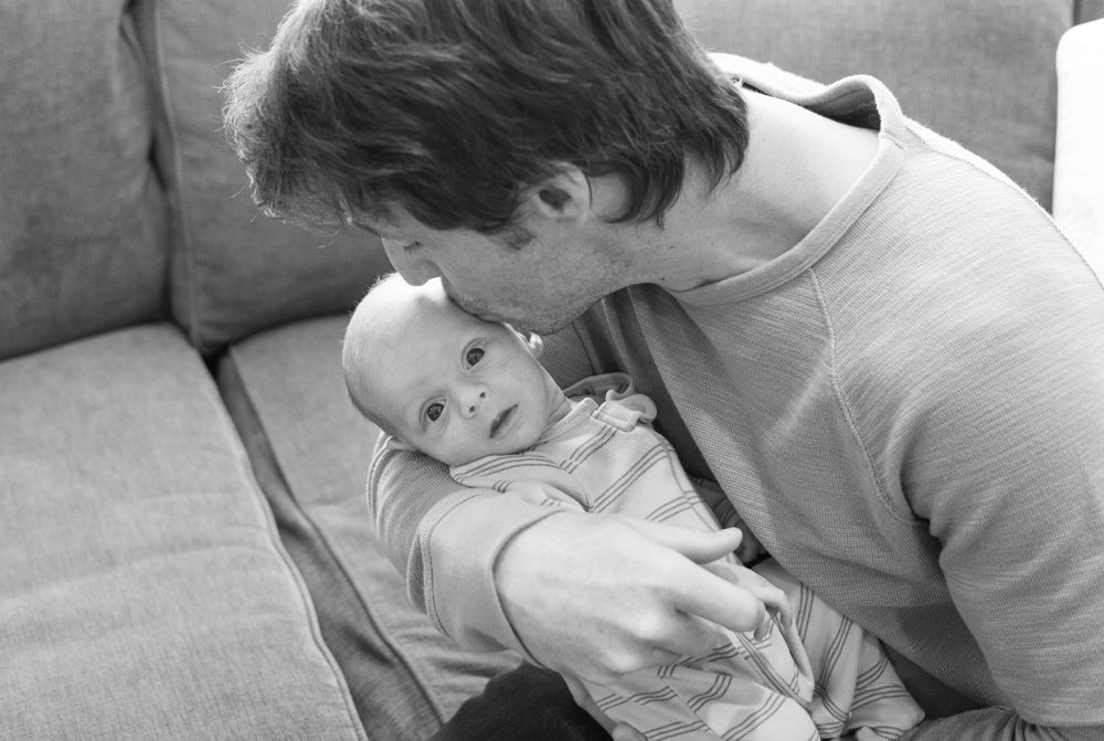 Black and white photo of parent sharing an intimate moment with infant on couch.
