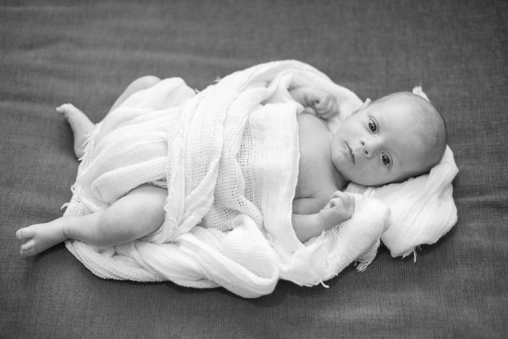 Black and white portrait of baby in white clothing lying on soft blanket.