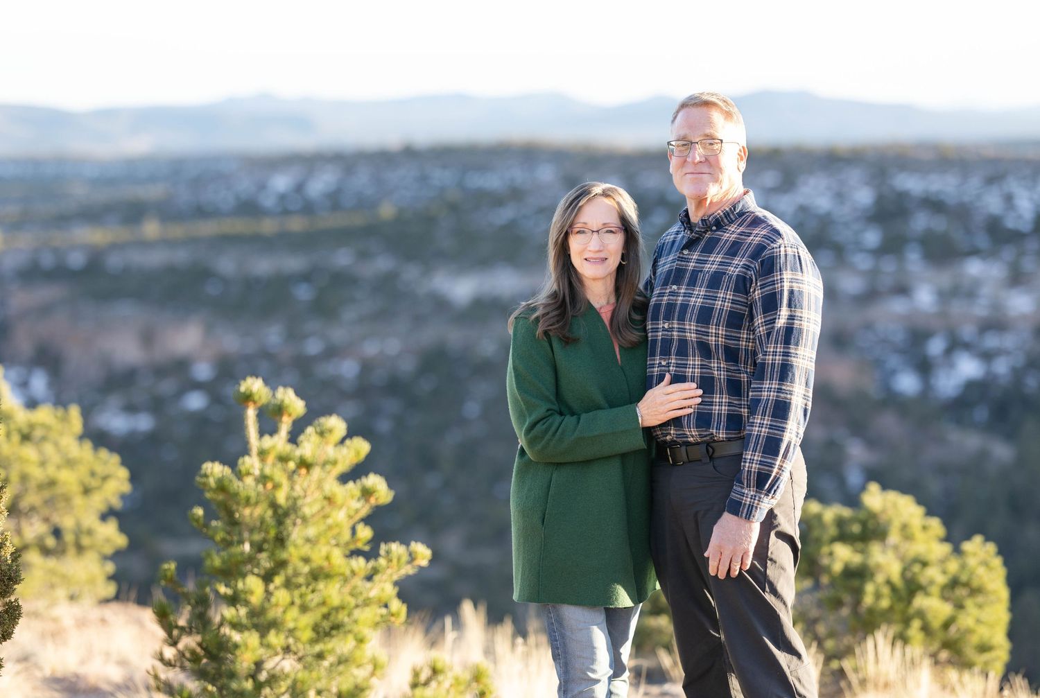 Couple poses together on hilltop overlook during golden hour in casual outdoor photo shoot.