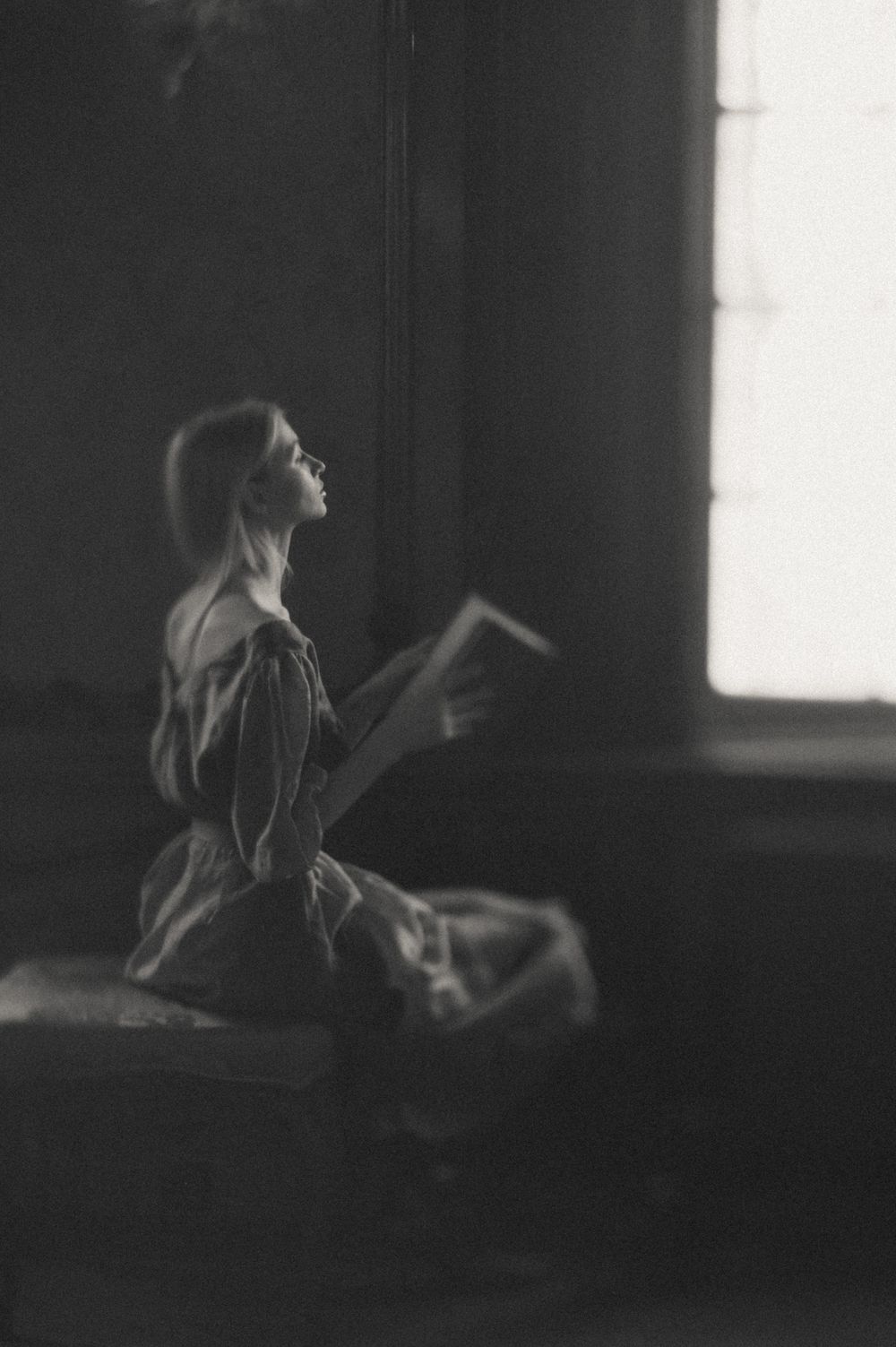Dreamy black and white silhouette of a person reading by a window in vintage style.