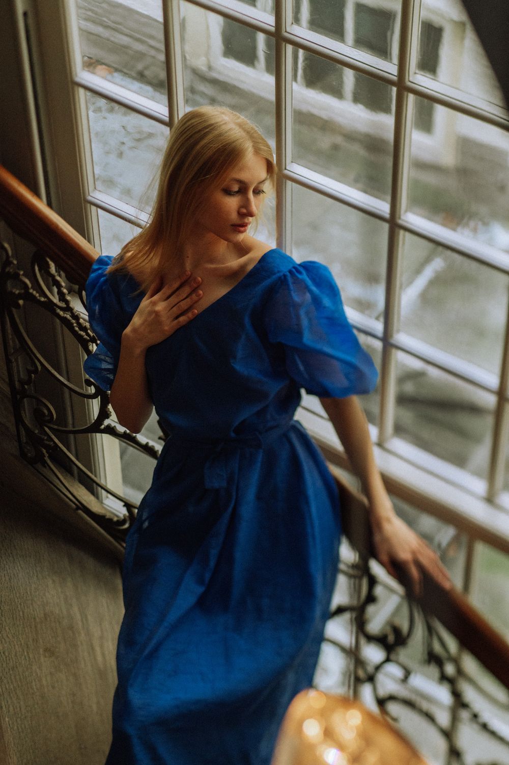 Artistic portrait with blue dress and dramatic window lighting in vintage interior.