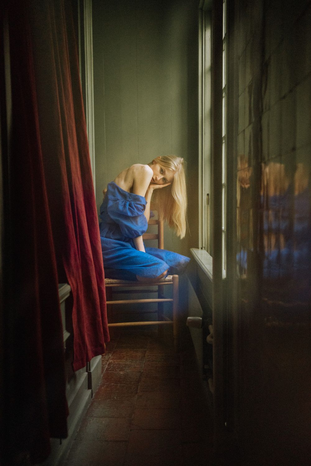 Moody corridor scene with figure in blue dress creating shadowy reflections.