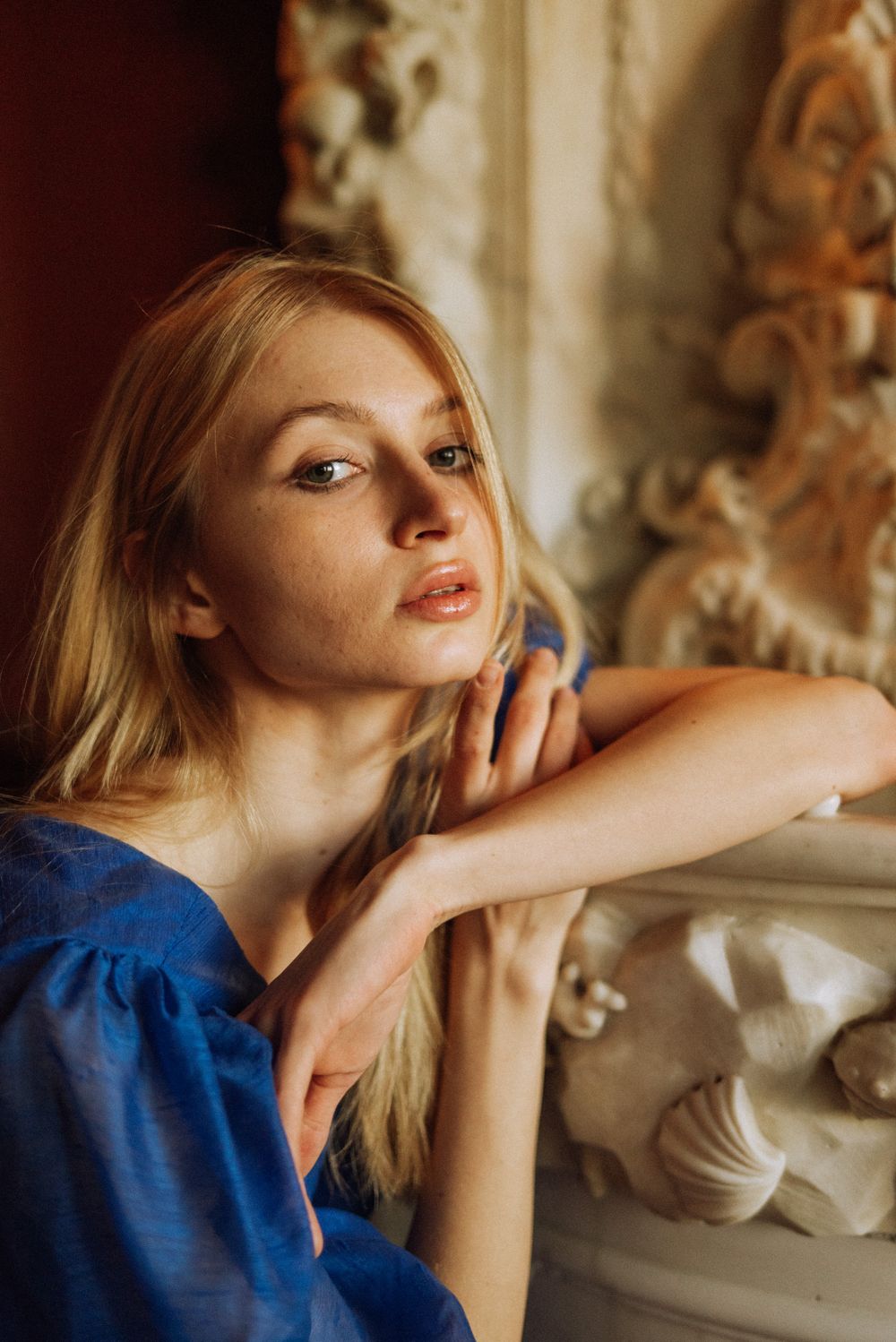 Artistic portrait of a woman in a blue dress posing against ornate architectural details in warm lighting.