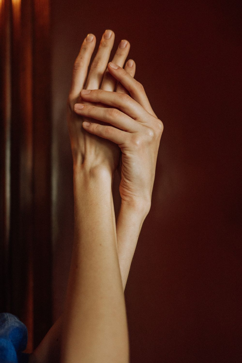 Elegant close-up of delicate hands gently touching against a dark burgundy background.