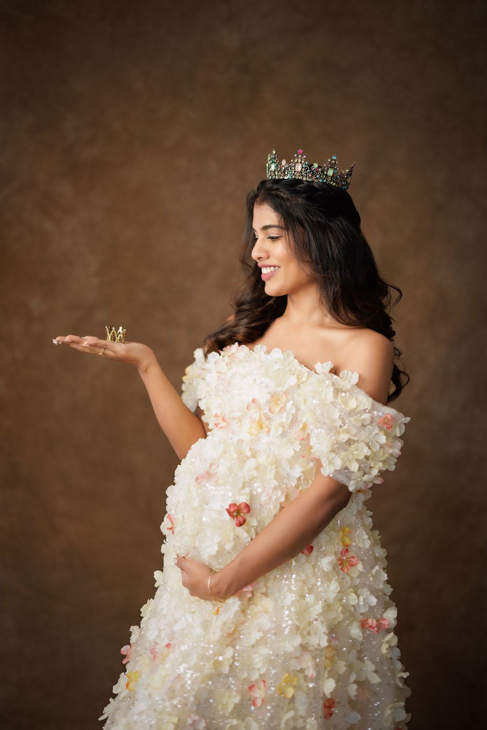 A whimsical maternity portrait in a textured cream gown with crown and playful pose.